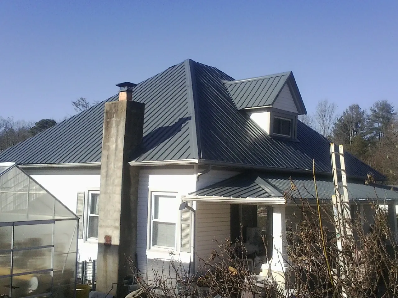 Dark blue standing seam metal roof on a white farmhouse with dormer — Slate & Tile Roof Repair by Roofing Brothers in Grosse Ile