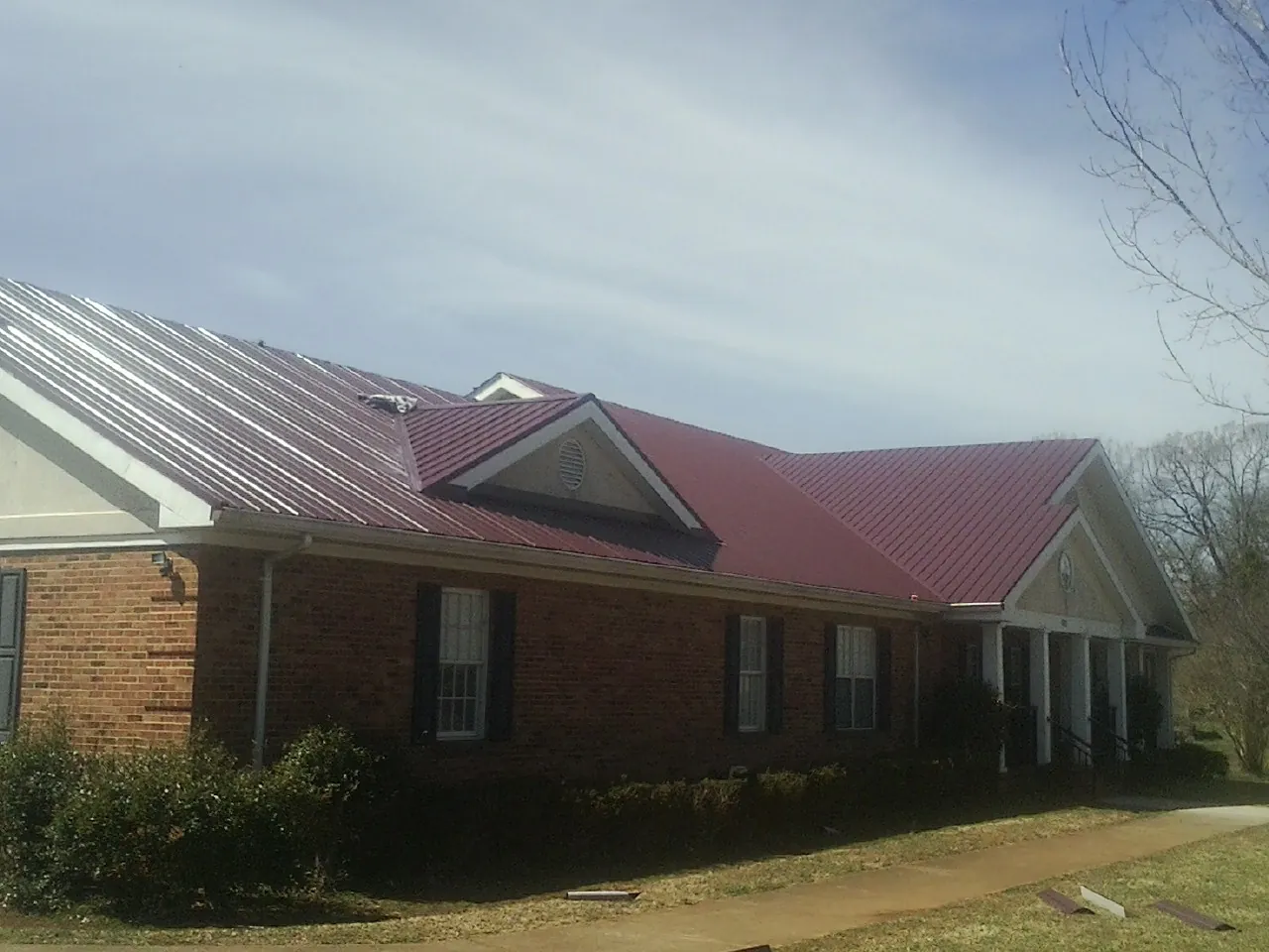 Red metal roof with gabled entries on a long brick building, from a Hail Damage Roof Repair job in Grosse Ile