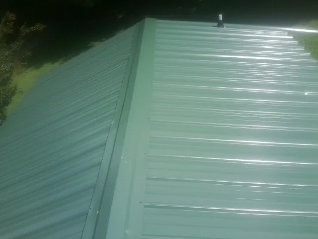 New green metal panels meeting at the ridge of a roof — Flat Roof Repair work by our crew in Grosse Ile