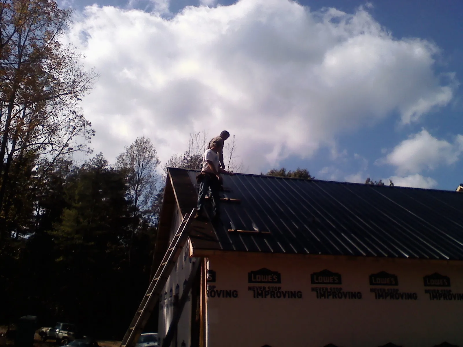Roofer fastening dark metal panels high against a cloudy sky, from a Roof Inspection job in Grosse Ile