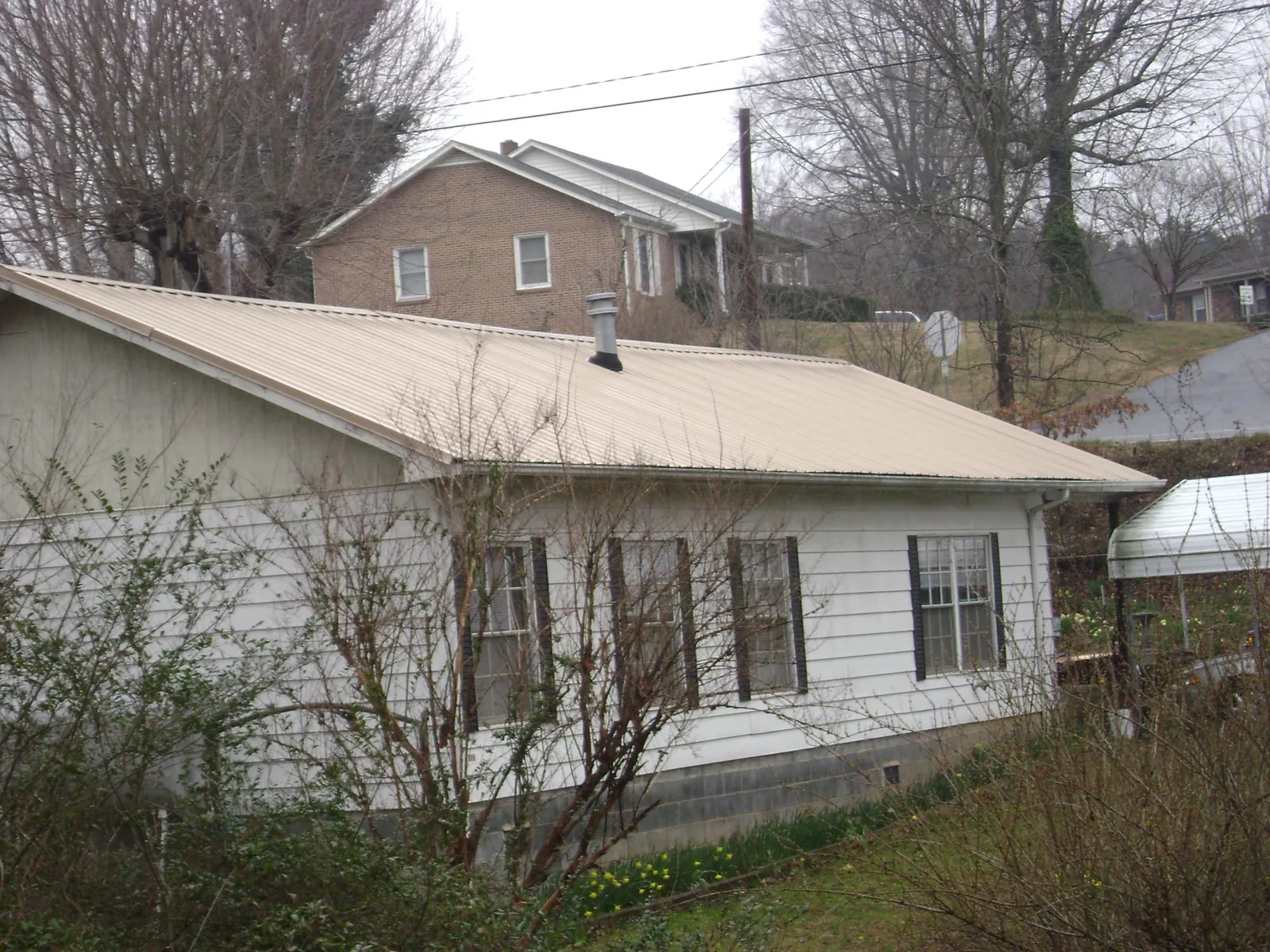 Tan metal roof on a white sided house set into a hillside — Commercial Roofing by Roofing Brothers in Grosse Ile